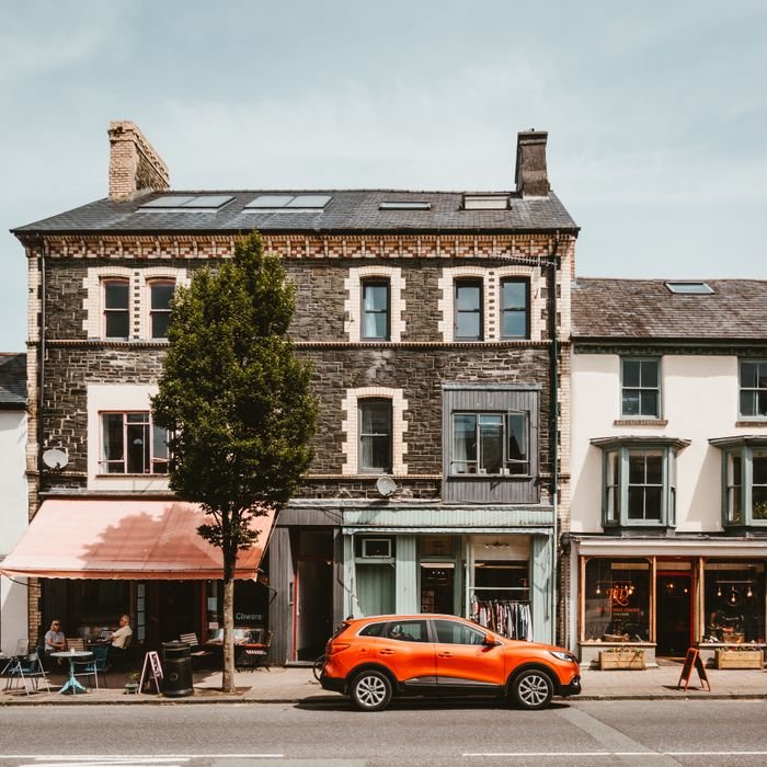 A vibrant street view in Machynlleth, featuring a café, colorful shops, and a parked car.